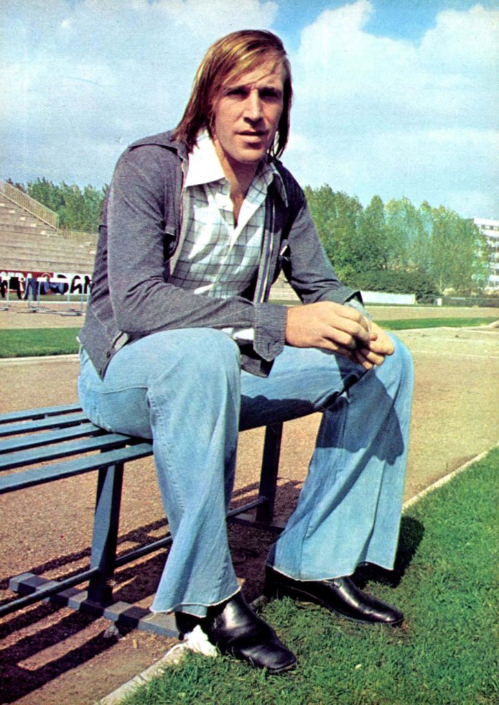 Vintage 1970s Günter Netzer German football legend in wide-leg jeans on stadium bench wallpaper
