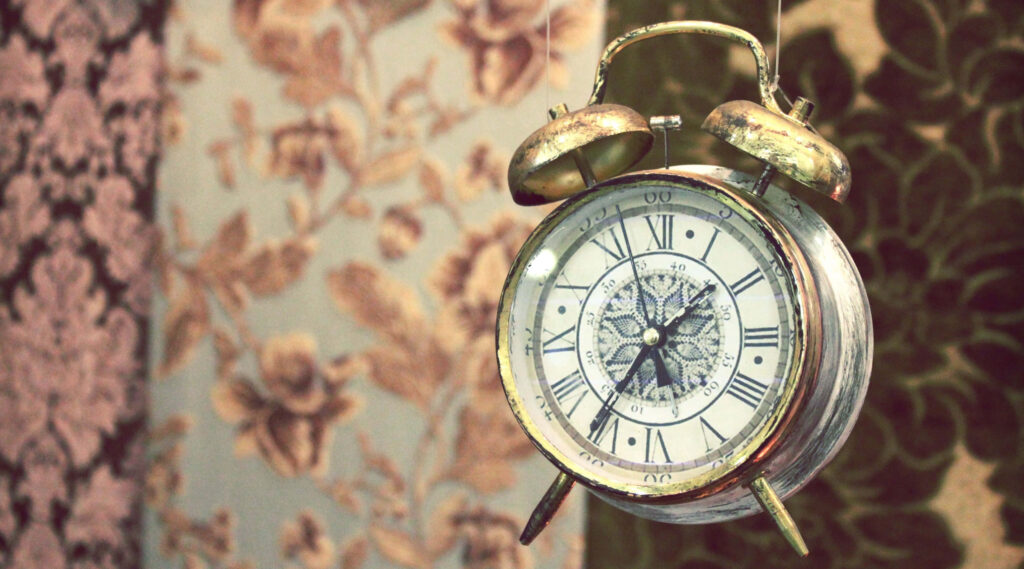 Vintage alarm clock hanging on floral patterned wallpaper with rustic elegant muted tones