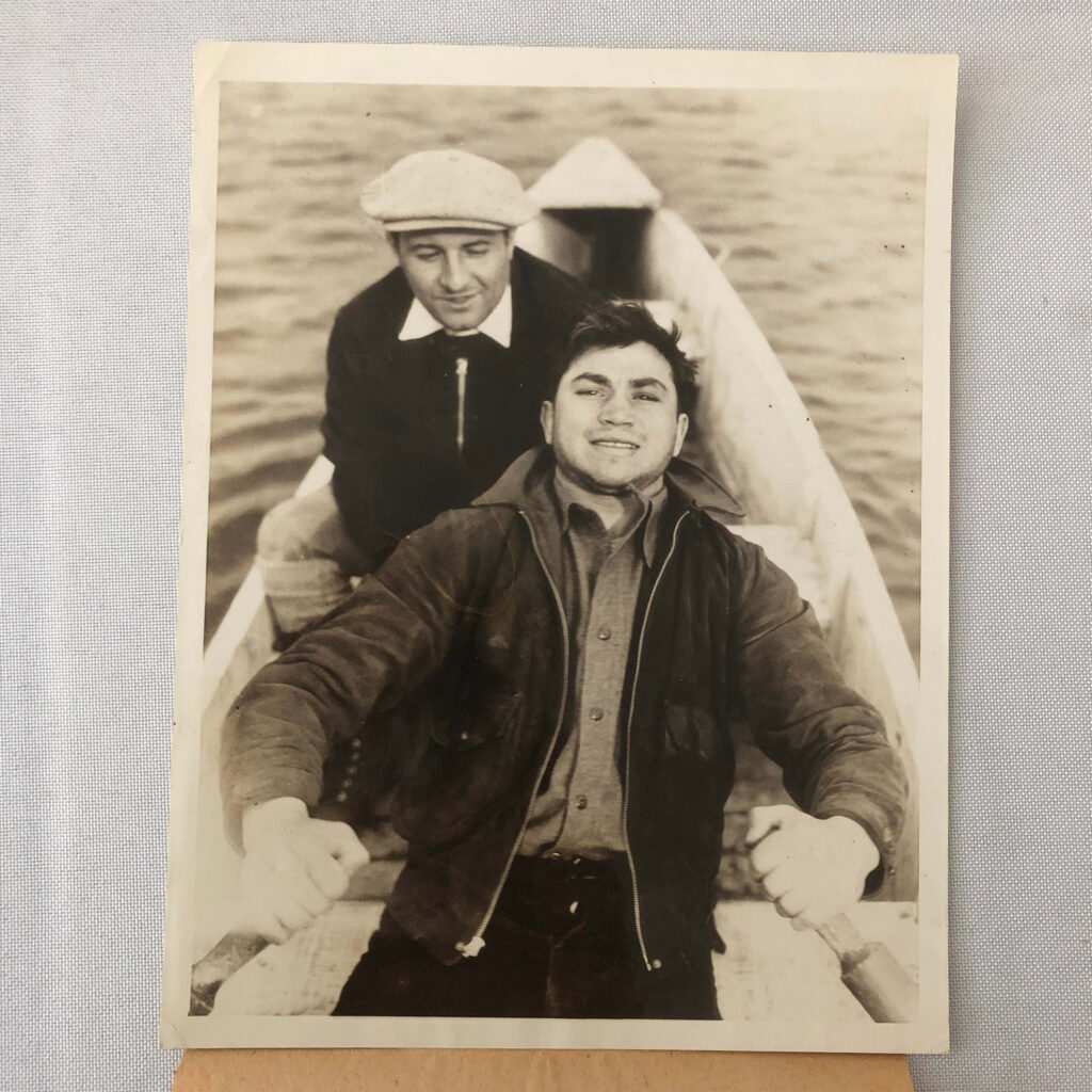 Vintage photo of Barney Ross rowing a boat smiling with a man behind on calm water background Wallpaper