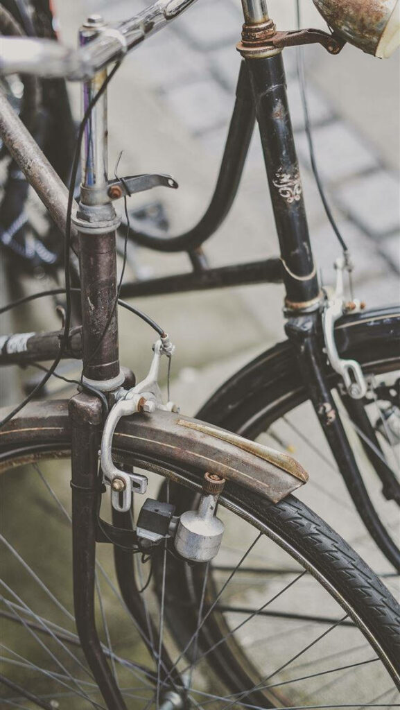 Close-up of two vintage bicycles with weathered metal frames on city street urban wallpaper background