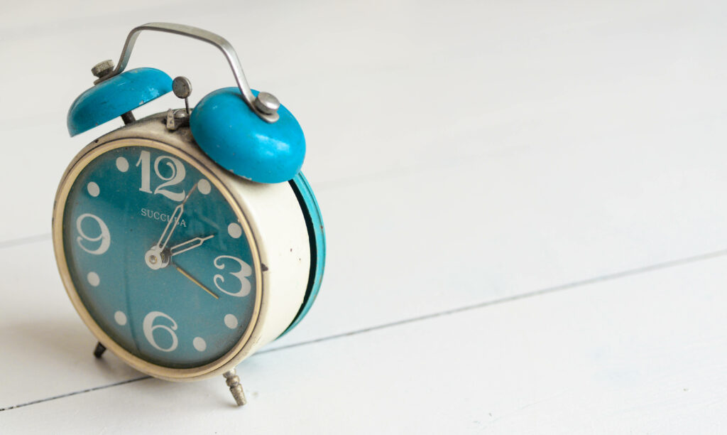 Vintage blue alarm clock with white numerals on light wooden background retro wallpaper