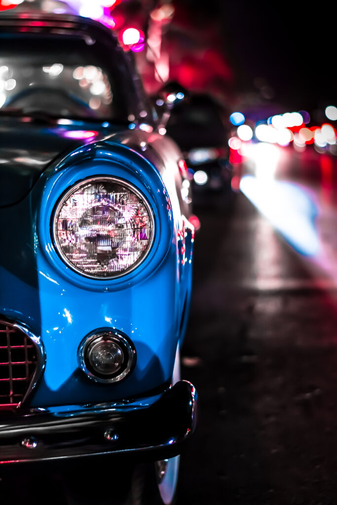 Vintage Blue Car Close-Up: Intricate Headlight Design & City Background Wallpaper
