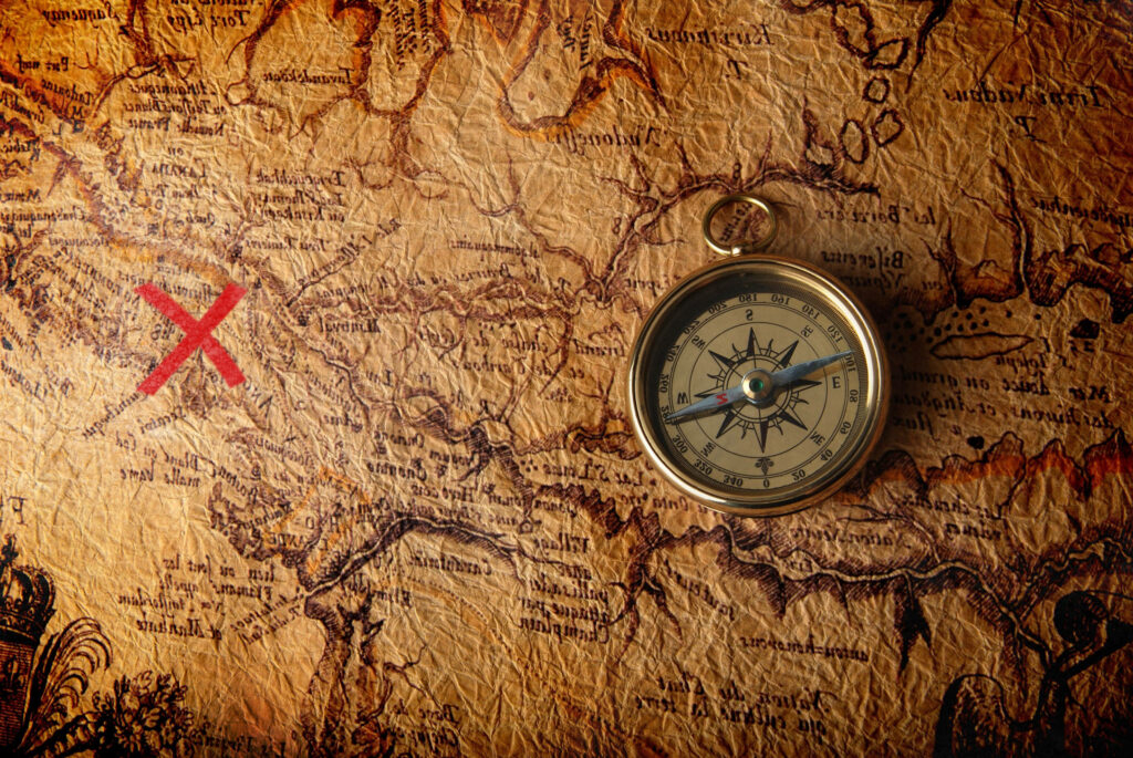 Vintage brass compass on ancient treasure map with red X adventure exploration wallpaper background