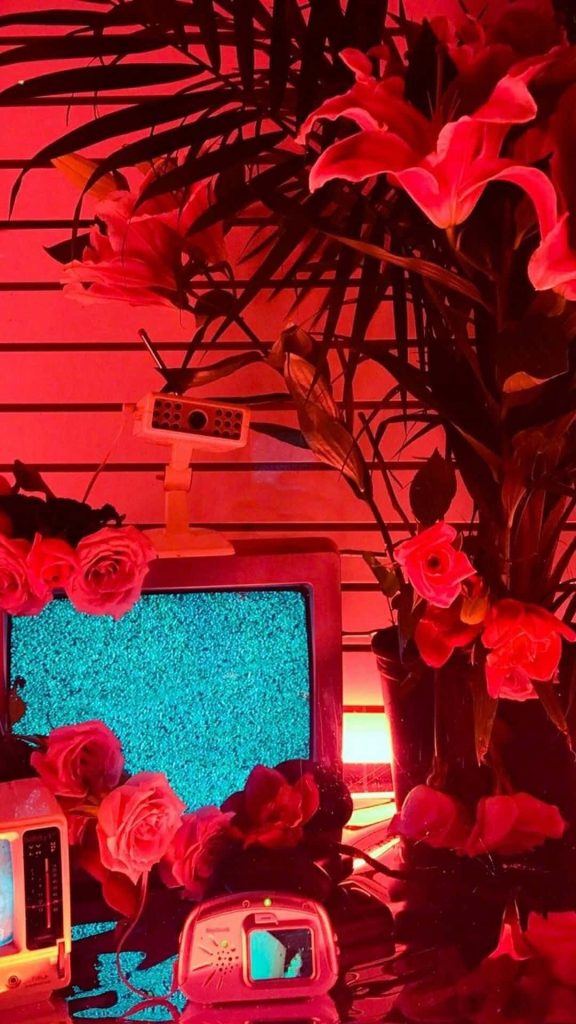 Vintage CRT monitor with static amid pink roses and lilies in neon red vaporwave wallpaper