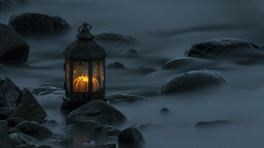 Vintage candle lamp glowing among smooth rocks by misty sea minimalist tranquil coastal scene Wallpaper
