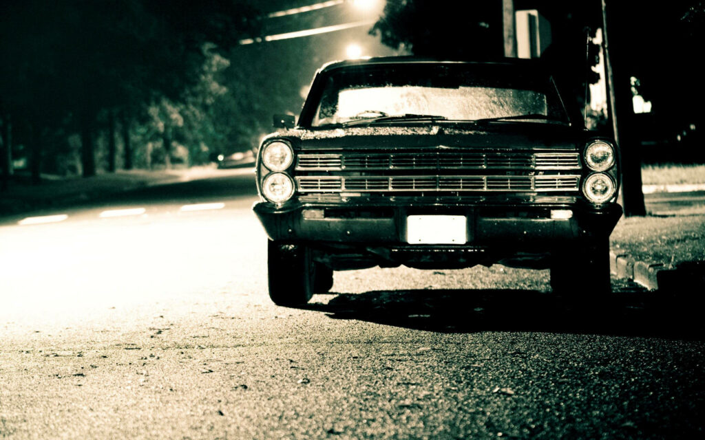 Vintage car parked on quiet street at night under soft streetlights peaceful nostalgic scene Wallpaper