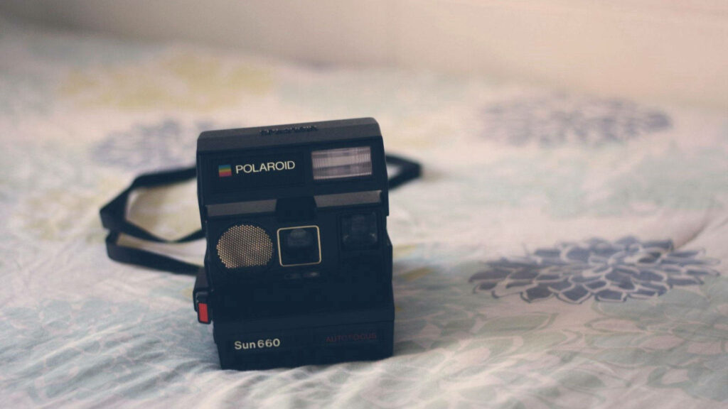 Vintage Polaroid Camera Resting on Floral Patterned Bed Sheet Wallpaper
