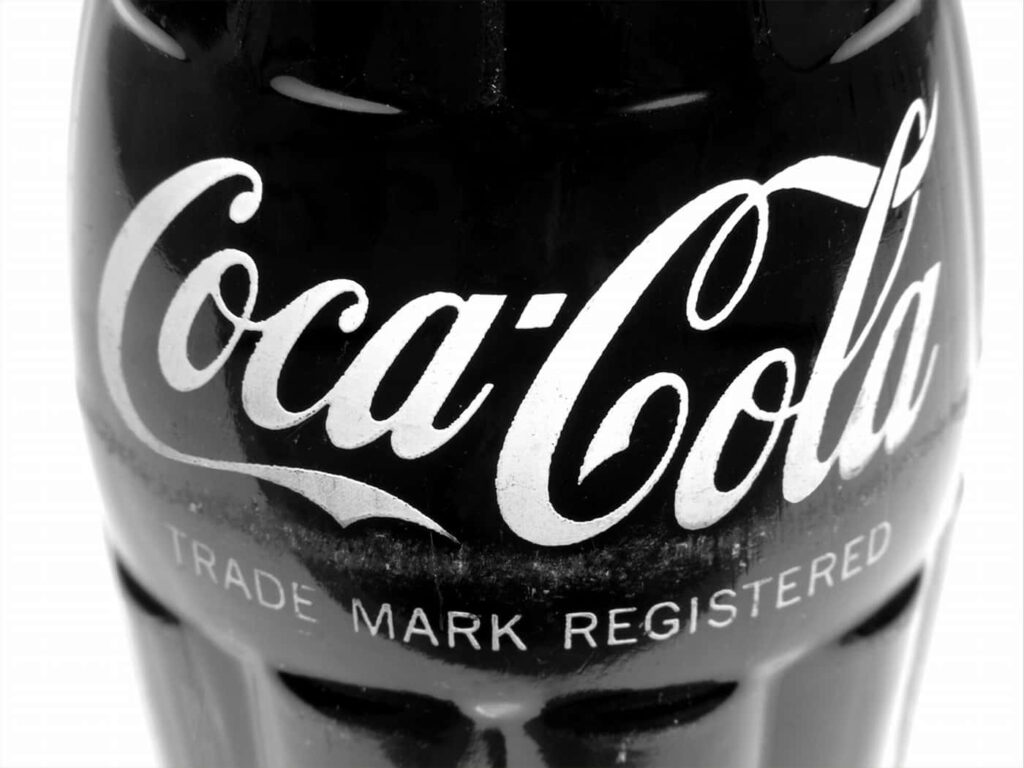Close-up of classic Coca-Cola glass bottle with white logo on glossy black vintage wallpaper background