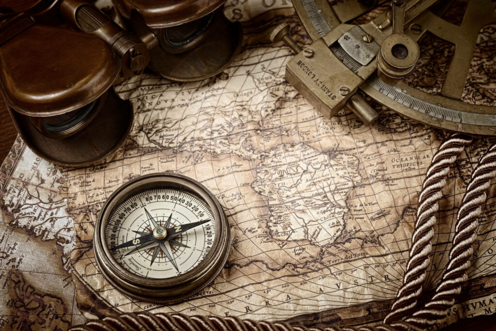 Vintage brass compass on antique map with nautical tools sepia wallpaper background adventure