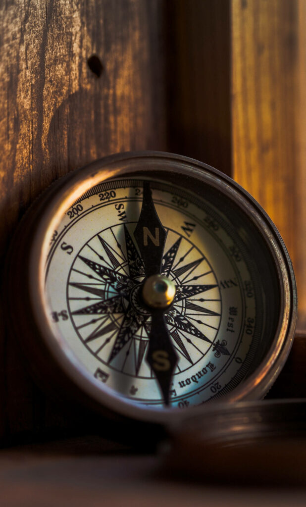 Vintage brass compass on warm wooden surface illuminated by soft golden light background Wallpaper