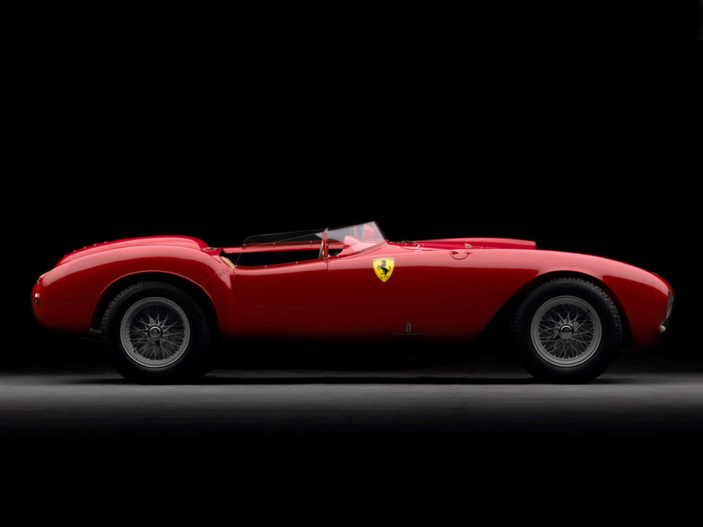 Vintage Ferrari 375 MM side profile with classic red paint and elegant wire-spoke wheels on black background Wallpaper
