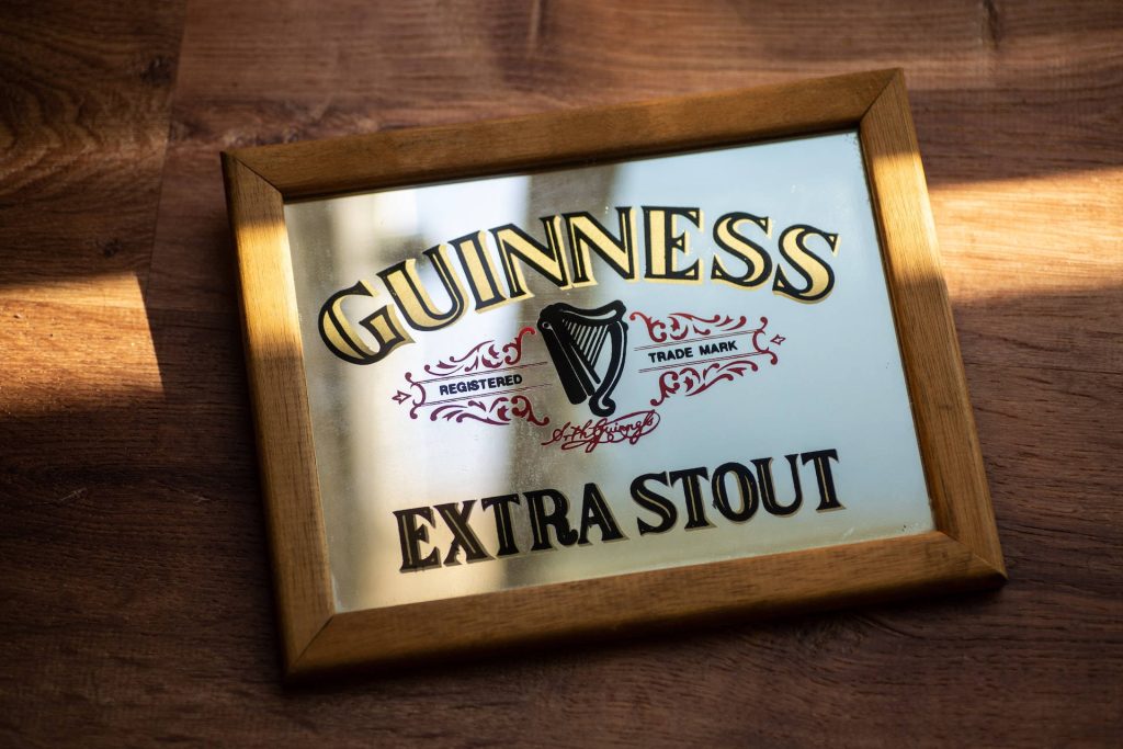 Vintage Guinness Extra Stout bar mirror wallpaper with iconic Irish harp logo and warm wood frame