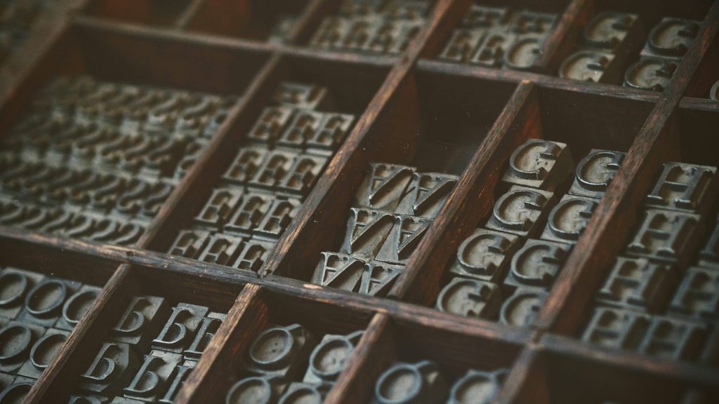 Macro shot of vintage letterpress metal type in wooden case with warm moody lighting background Wallpaper