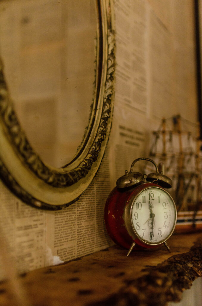 Vintage red alarm clock reflected in antique mirror on textured wall with old newspaper wallpaper