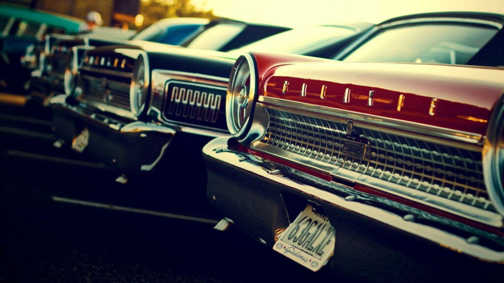 Vibrant red classic car with chrome details parked among vintage vehicles retro wallpaper background