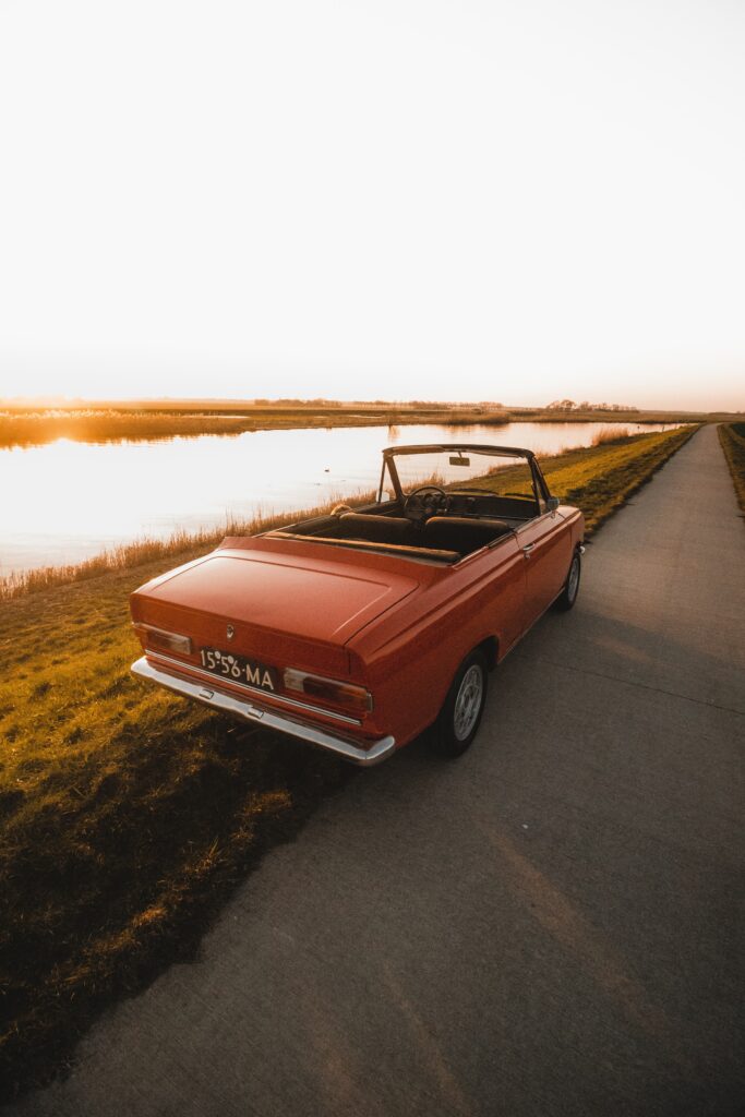 Vintage Red Convertible Wallpaper: Nostalgic Riverside Sunset Scene