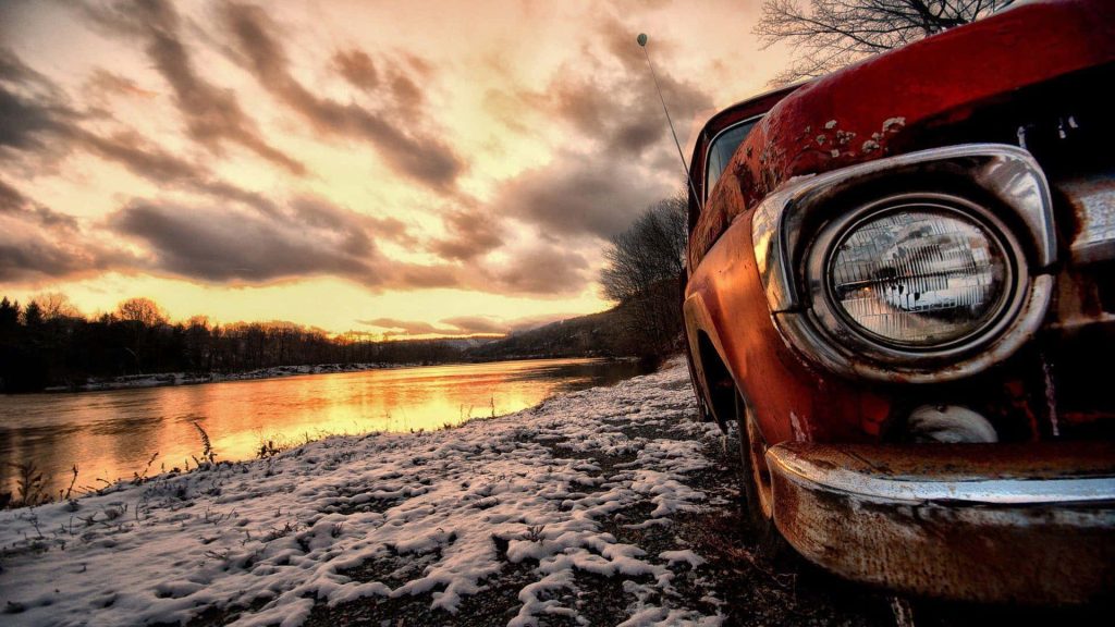 Vintage red pickup truck parked snowy riverside winter sunset rustic landscape wallpaper background