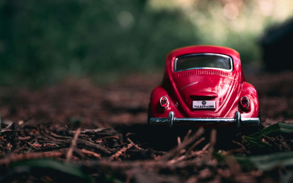 Vintage Red VW Beetle Toy Car Wallpaper on Rustic Earthy Surface