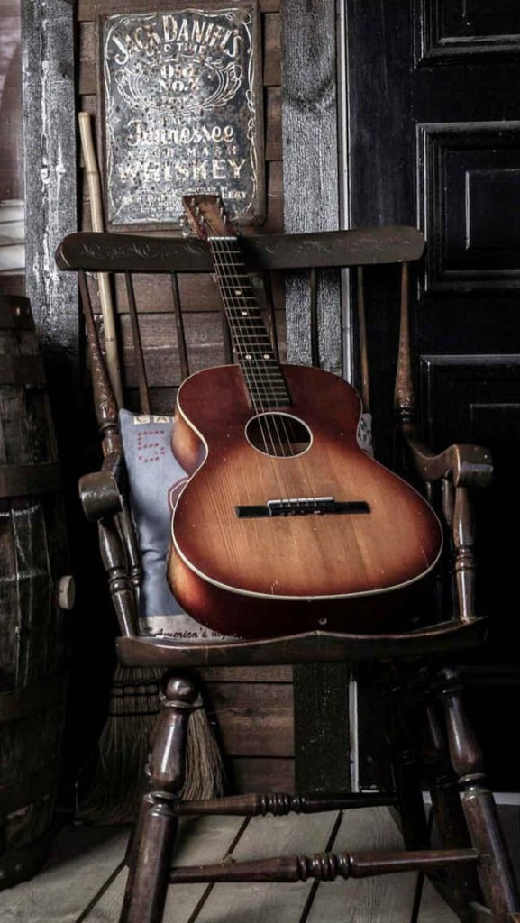 Vintage sunburst acoustic guitar on rustic rocking chair with Jack Daniel’s whiskey sign background Wallpaper