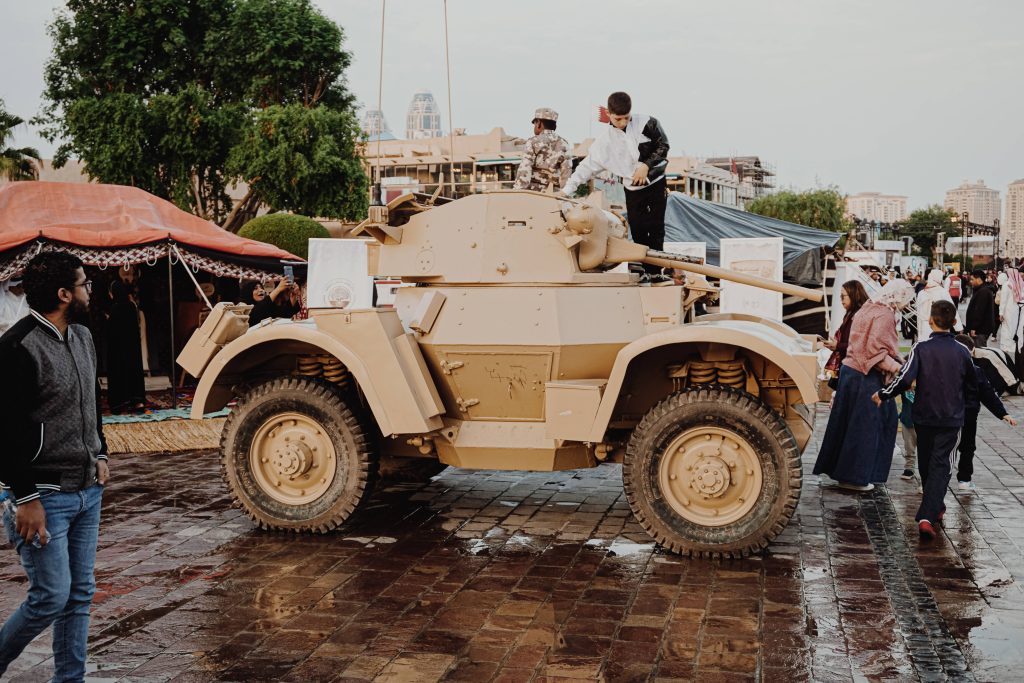 Vintage T17E1 Staghound armored car with tan exterior and child exploring turret in square Wallpaper