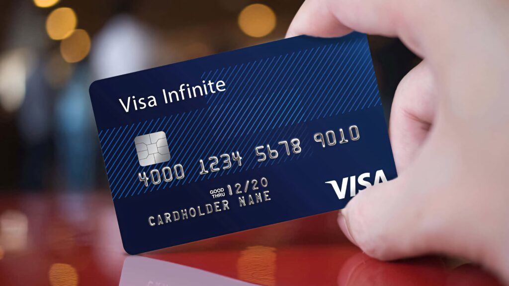 Hand holding sleek Visa Infinite credit card blue modern design silver details blurred red background Wallpaper
