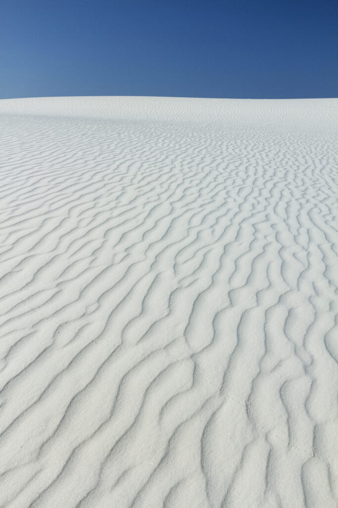 White desert dunes with wavy sand patterns under a clear vivid blue sky minimalistic wallpaper
