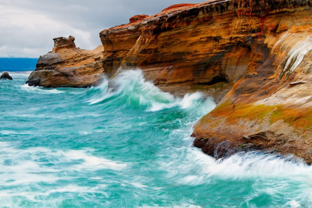Vivid blue ocean waves crash on rugged coastal rocks under bright sky high resolution wallpaper background