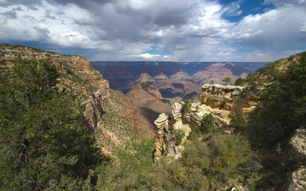 Vast canyon landscape with rugged mountains green shrubs and dramatic cliffs under blue sky Wallpaper