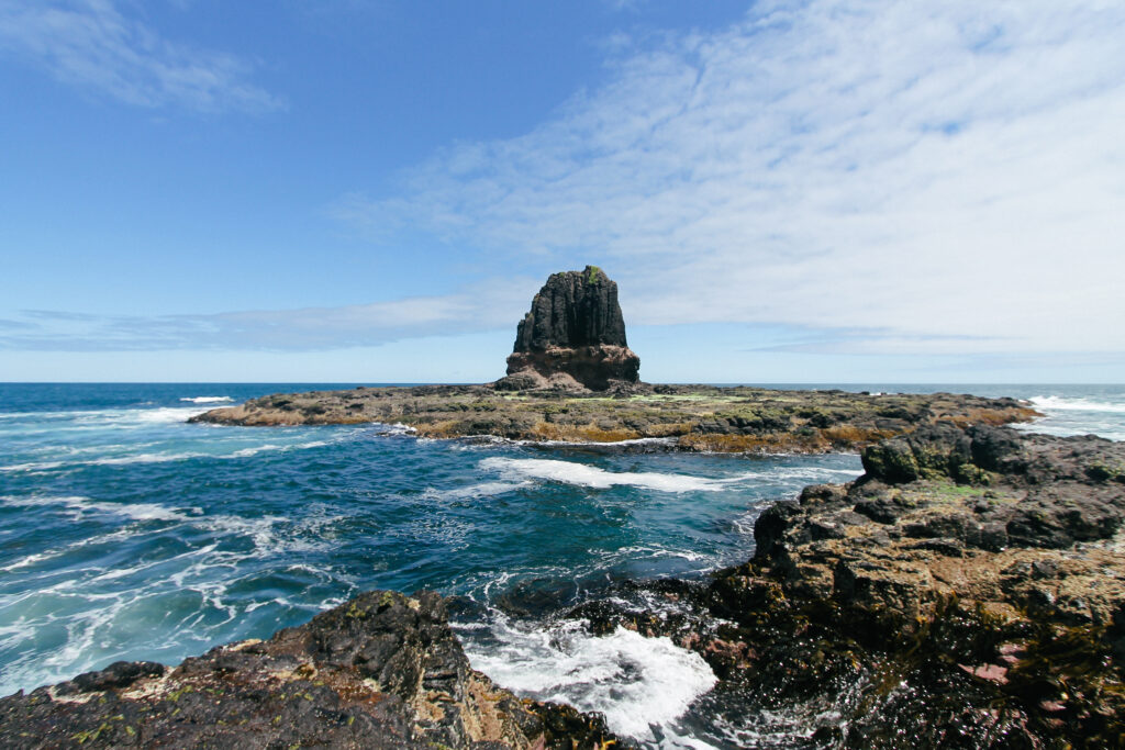 Vivid coastal wallpaper with rugged rocks turquoise sea waves crashing sea stack under blue sky