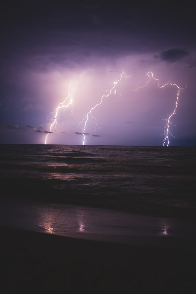 Vivid lightning bolts strike dark restless sea at night with purple blue overcast sky wallpaper