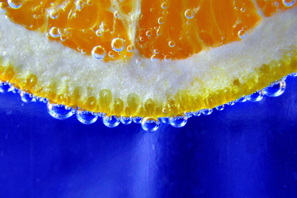 Vibrant Orange Slice Close-Up with Water Drops on Blue Wallpaper