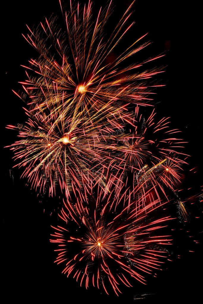 Vivid orange fireworks exploding in dark night sky festive wallpaper background bright celebration