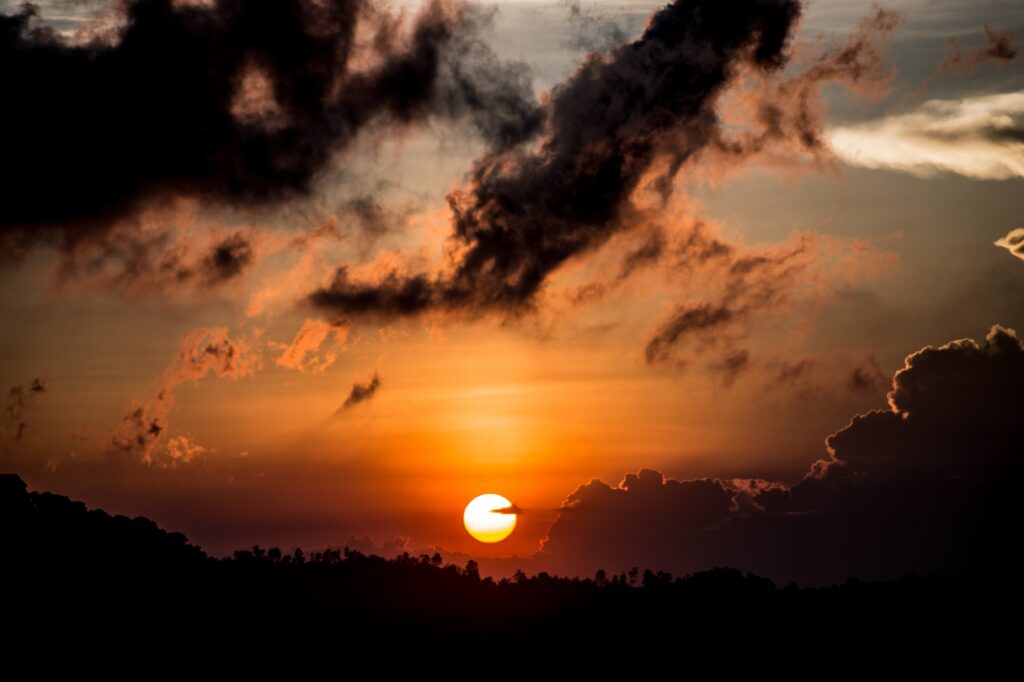 Vivid orange sunset with dark clouds and distant hills silhouette stunning wallpaper background