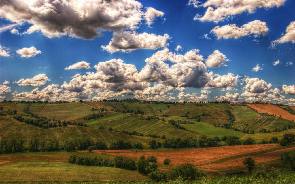 High-resolution landscape wallpaper with rolling mountains and patchwork fields under dramatic clouds