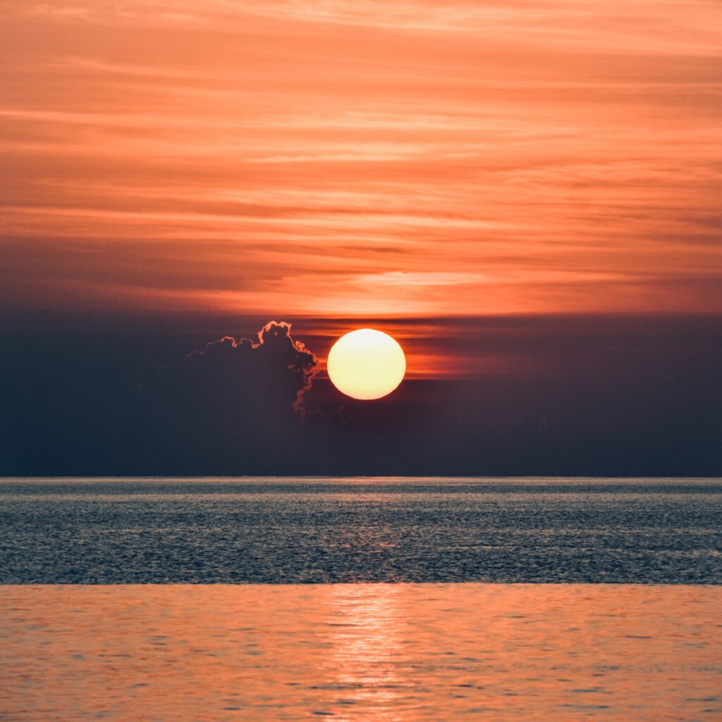Vivid sunset over calm sea with warm orange red sky and wispy clouds peaceful evening wallpaper