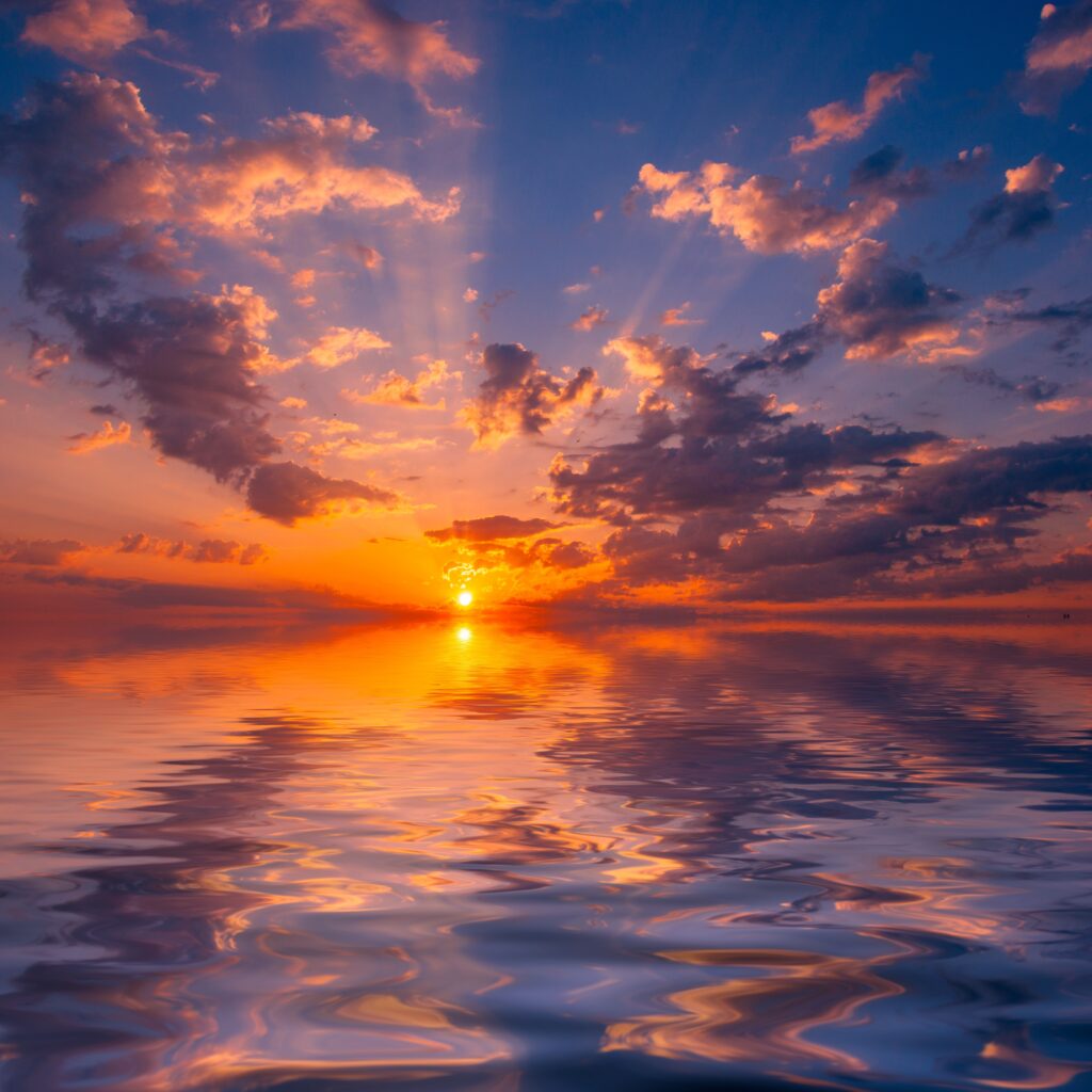 Vivid sunset over calm sea with golden light reflecting on rippling water and colorful clouds Wallpaper