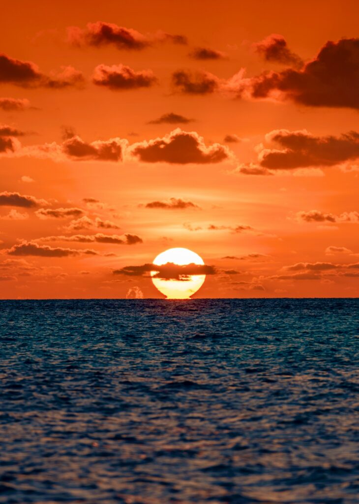 Vivid sunset over calm sea with orange red sky and scattered clouds serene seascape wallpaper