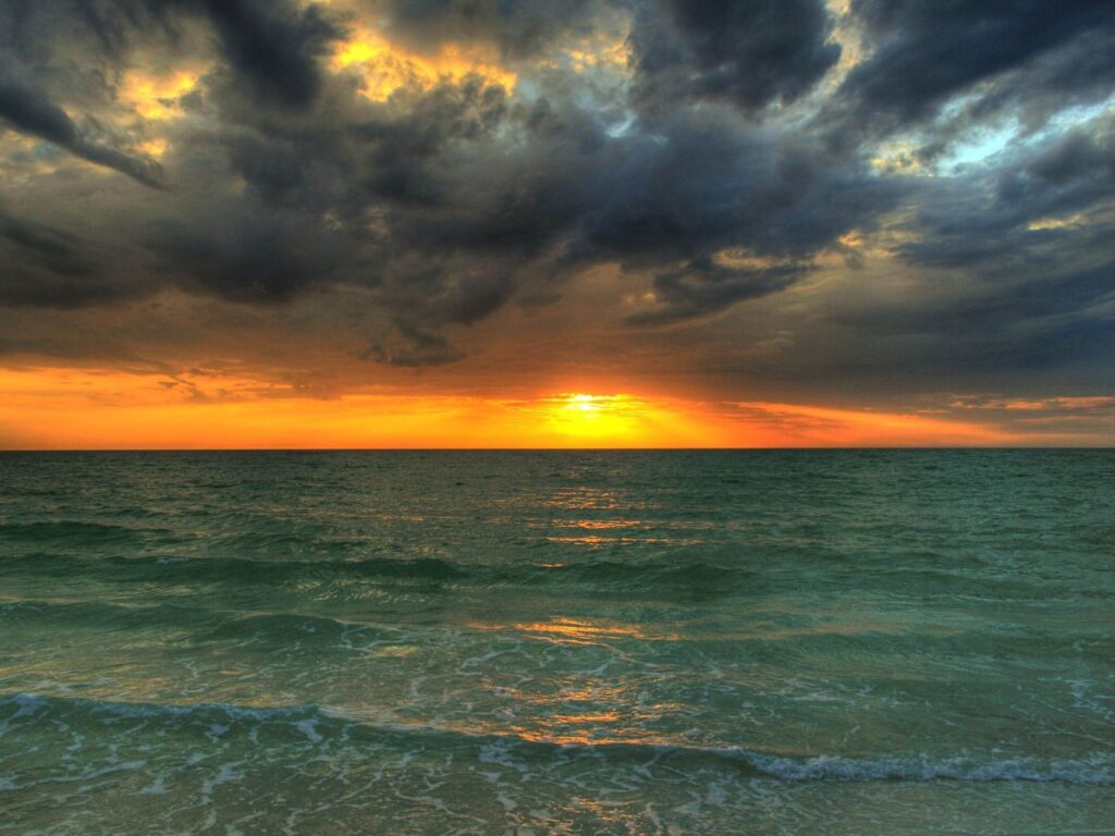 Vivid sunset over sea with dramatic clouds rolling waves and vibrant blue to orange colors wallpaper