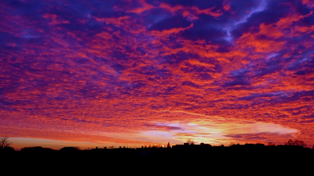 Vivid sunset with purple orange yellow clouds over silhouetted landscape serene wallpaper background