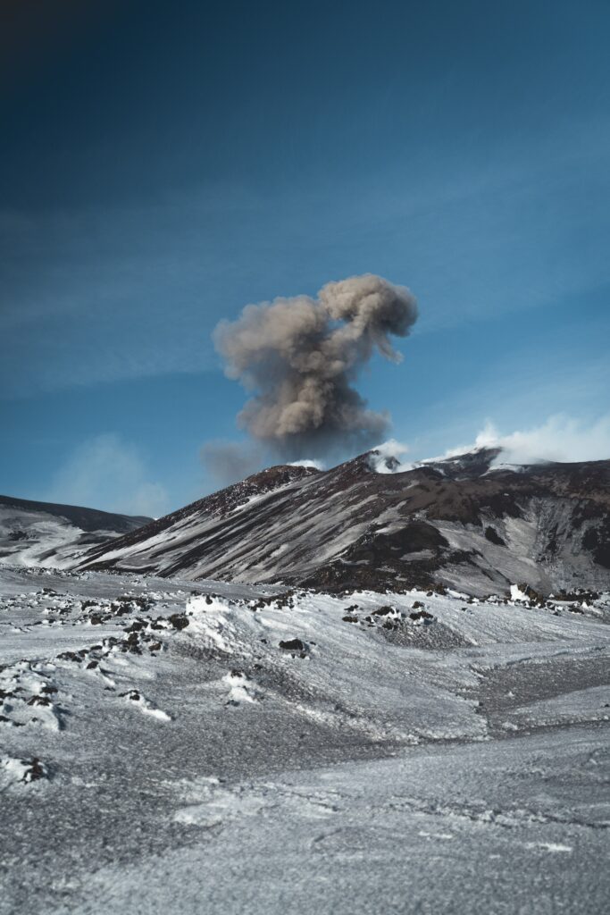 Volcanic mountain erupting with ash clouds under clear blue sky rugged ash-covered landscape Wallpaper
