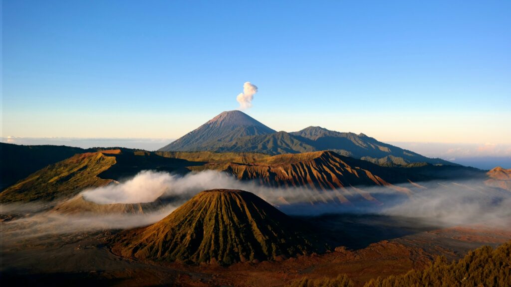 Volcanic landscape wallpaper with smoky volcano blue sky misty rugged peaks high-resolution scene