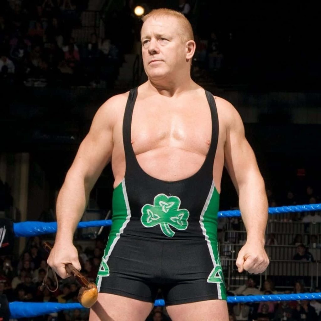 WWE legend Fit Finlay in black green singlet with shamrock holds wooden shillelagh in ring Wallpaper