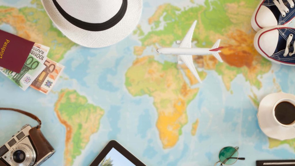 Top-down travel flat lay with passport euros camera hat sneakers on world map background Wallpaper