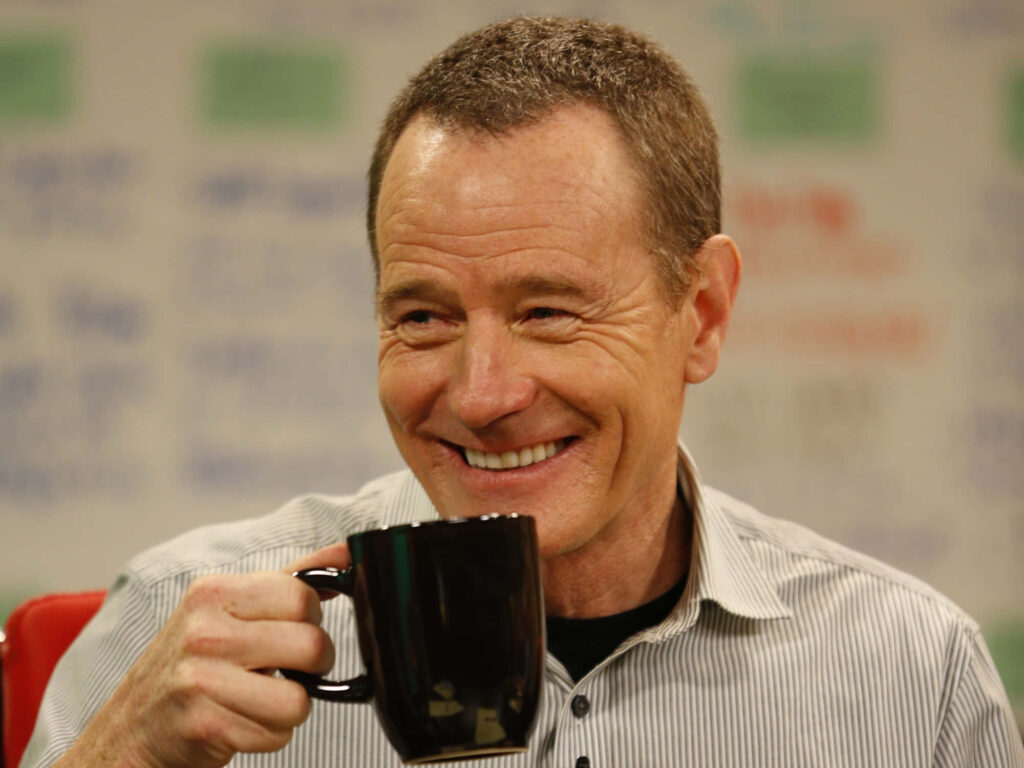 Bryan Cranston smiling warmly holding black coffee mug colorful blurred background wallpaper