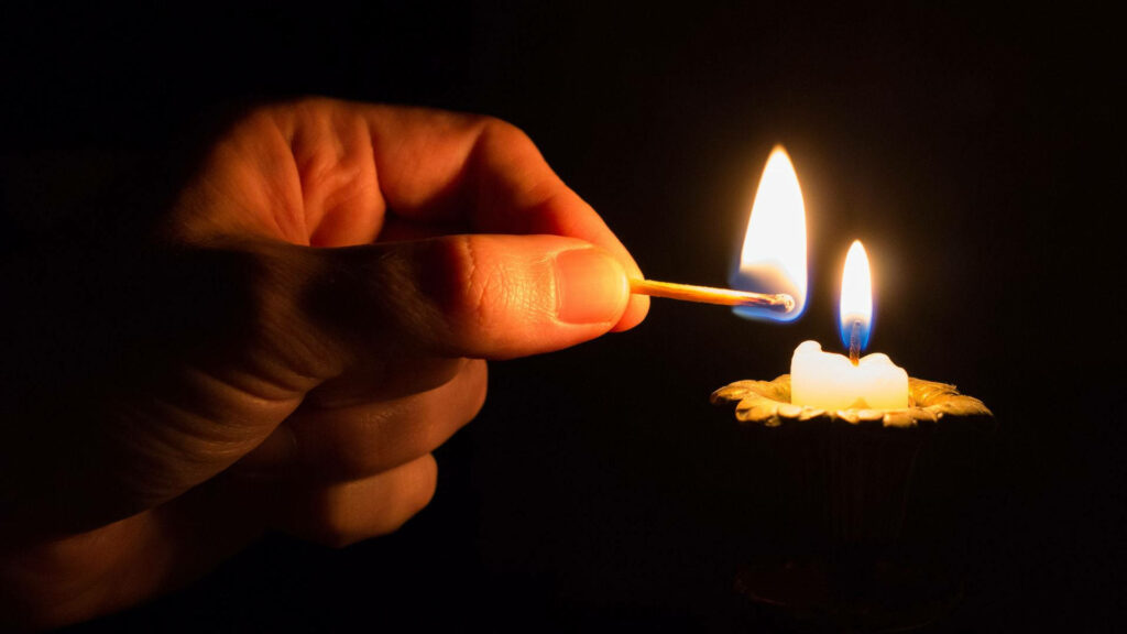 Close up of a candle flame lit by matchstick with warm golden light and soft blue shadows background Wallpaper