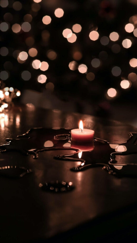 Warm glowing candle on reflective table with water drops and cozy brown gold bokeh background Wallpaper