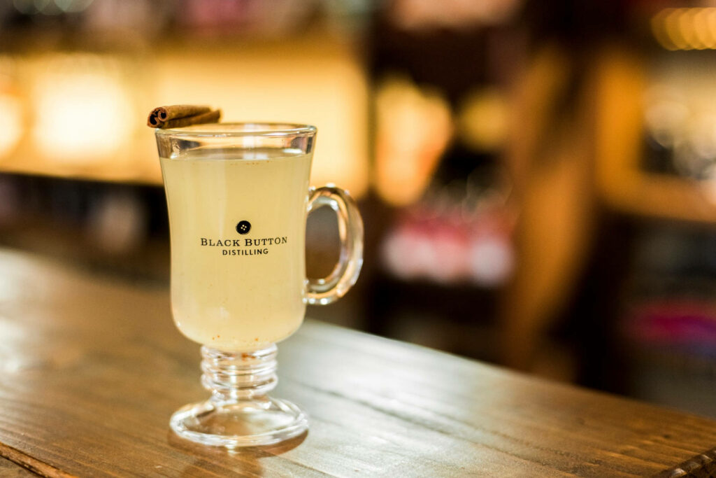 Cocktail glass with warm cinnamon drink on wooden bar at Black Button Distilling nightlife ambiance Wallpaper