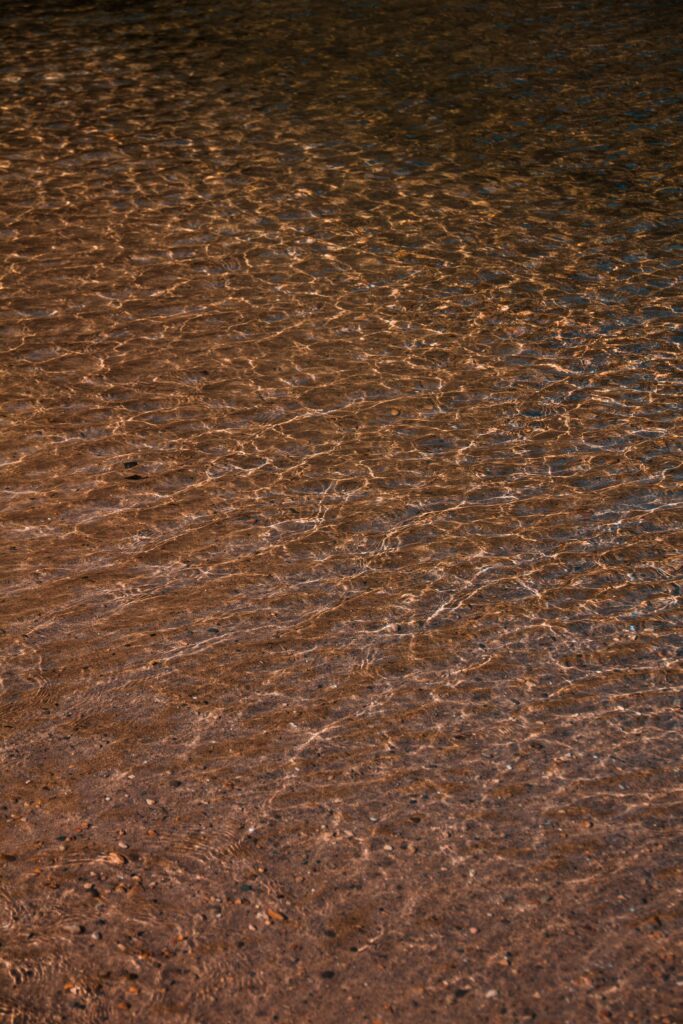 Warm sunlight shimmering on shallow water with ripples over sandy ground natural background Wallpaper