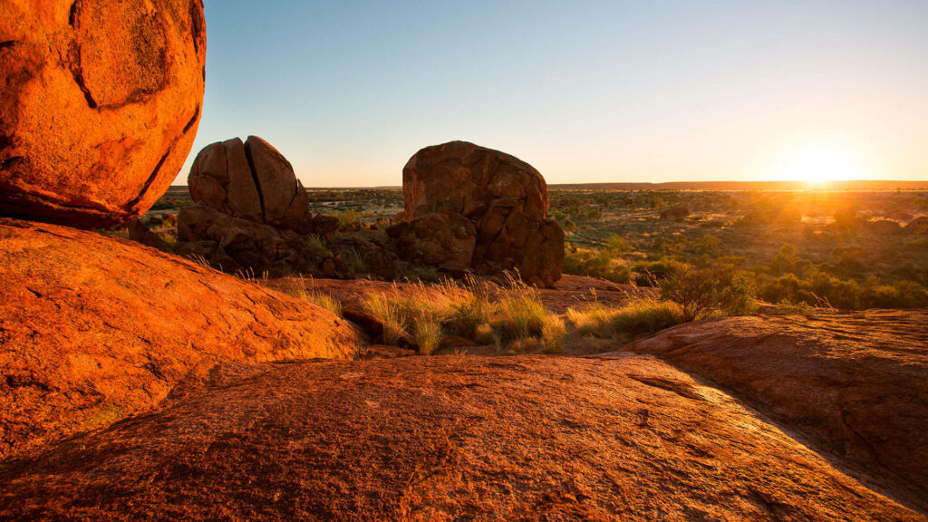 Warm sunlight on rugged Australian Outback rocks and sparse vegetation under clear sky wallpaper