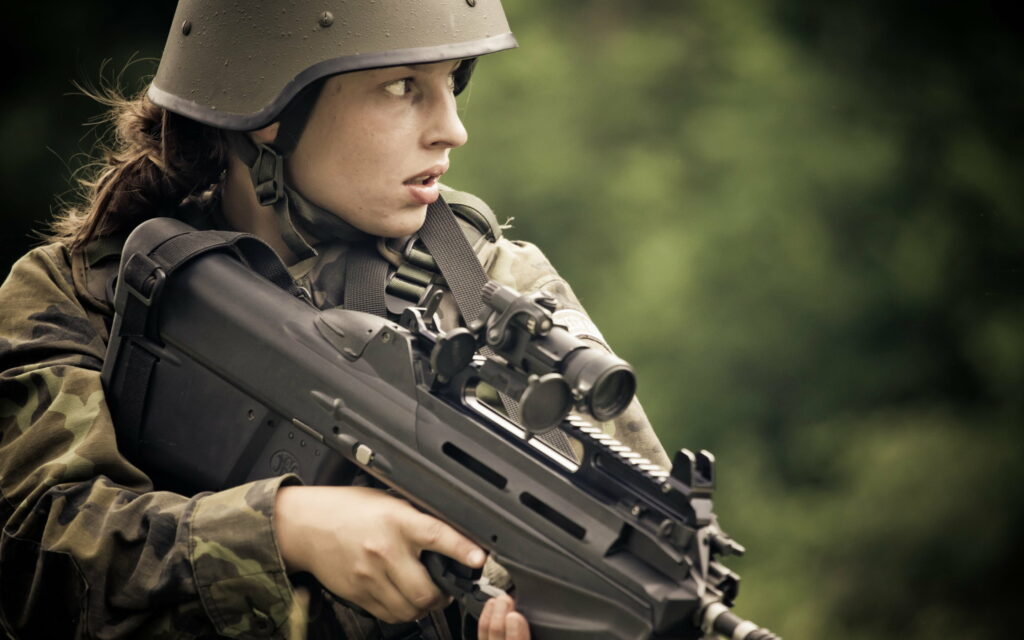 Battle-Ready Maiden: Enchanting Soldier with FN F2000 Assault Rifle in Vibrant War Zone Wallpaper
